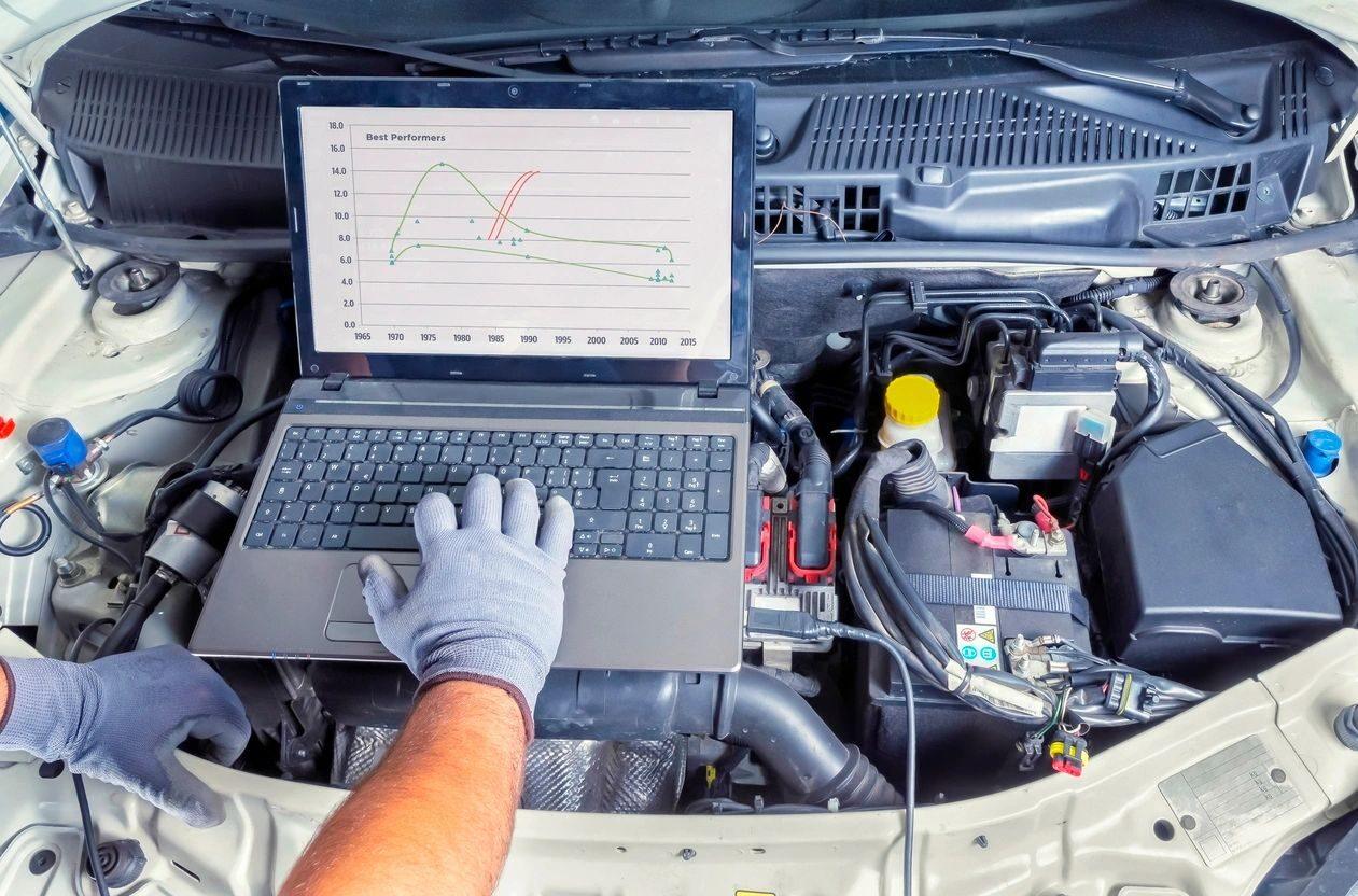 Mechanic analyzing car engine data on laptop.