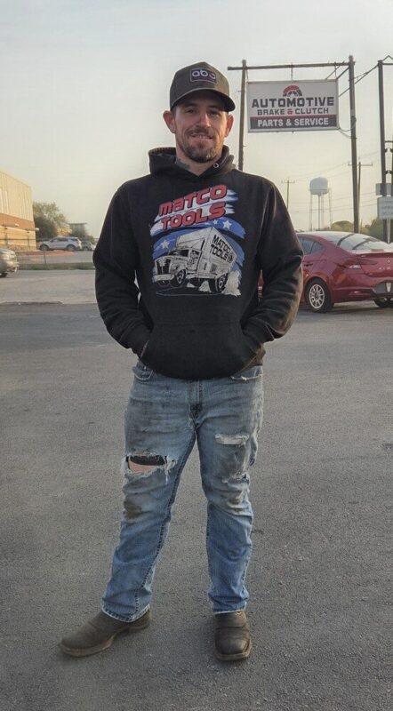 Full body photo of Taylor Murphy, Fleet Mechanic, standing in front of Automotive Brake & Clutch shop, ready to perform comprehensive brake repair and transmission overhauls on commercial trucks.